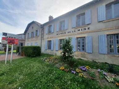 La façade du Musée de la Mine avec un parterre de fleurs et un panneau indiquant Musée de France